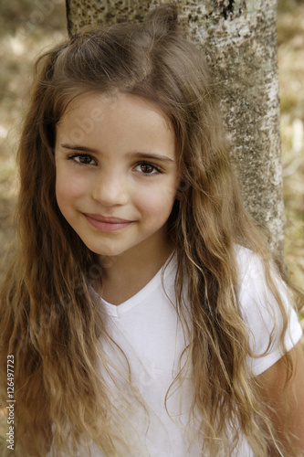 young girl leaning against tree trunk