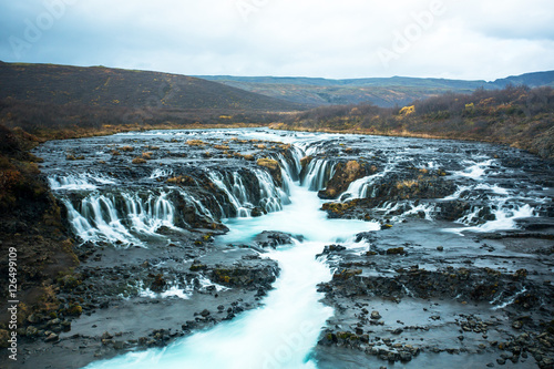 Bruarfoss or waterfall bridge, consists of numerous runlets falling into a chasm at the middle. At the chasm, the water of Bruara river is colored in glacial blue running on black volcanic bedrock.