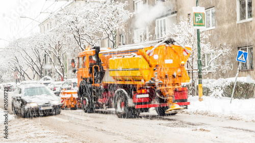 city street covered with snow during heavy winter storm in one European capital city, vehicles defocused due to its movement, snowplough shoveling roads