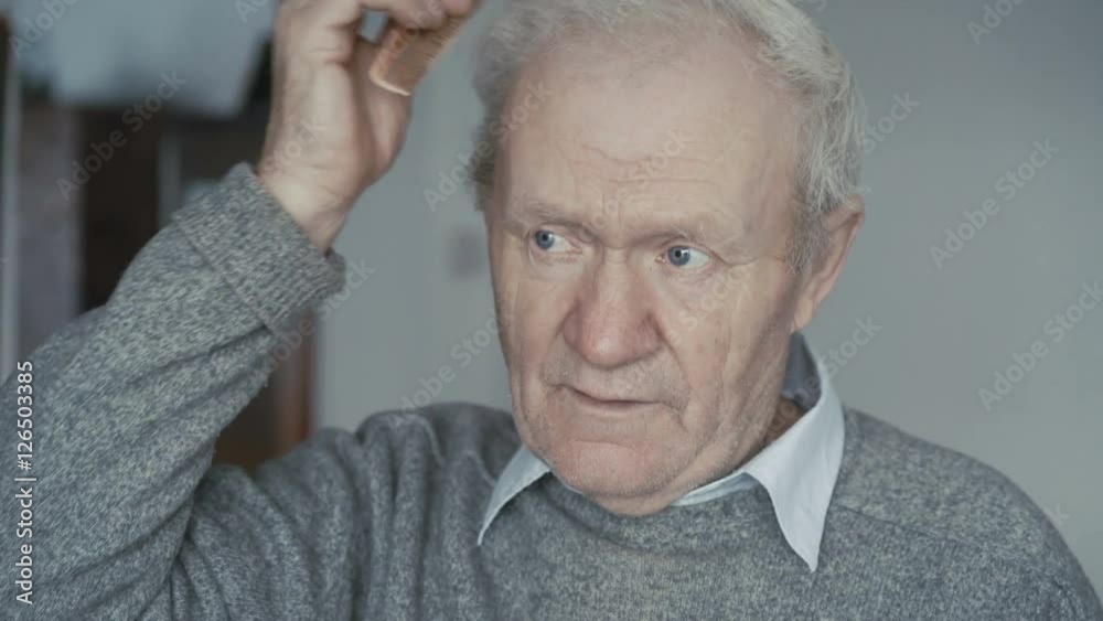 Senior is combing his short gray hair with a wooden comb 4K