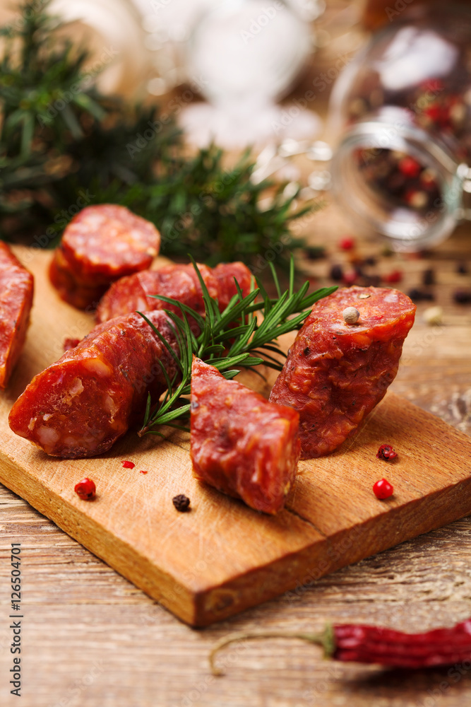 Delicious smoked sausage, sliced on a wooden board with spices.