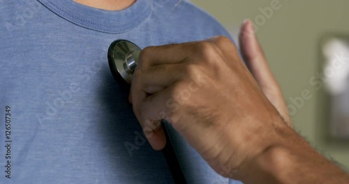 Doctor's hands using stethoscope to examine a female patient in hospital examining room. Close up detail shot.