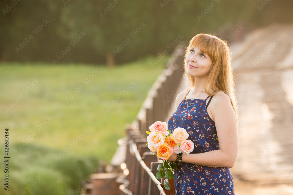 Young girl with a bouquet of roses standing on the bridge in the background blurred foliage Young girl with a bouquet of roses standing on the bridge in the background blurred foliage