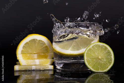 Falling in a glass of lemon, lime, splash on black background, isolated, water drop