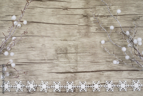 Ein Holzuntergrund mit Schneekristallen am unteren Bildrand und Zweigen mit kleinen Schneebällen rechts und links, horizontal mit Textfreiraum photo