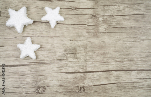 Ein Holzuntergrund mit drei Sternen aus Schnee am linken Bildrand, horizontal mit Textfreiraum