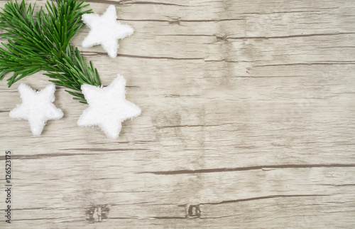 Ein Holzuntergrund mit drei Sternen aus Schnee und einem Tannenzweig am linken Bildrand, horizontal mit Textfreiraum