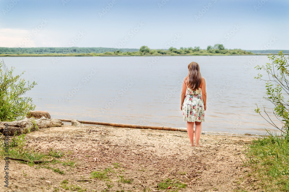 Girl brunette stands on the river bank in sundress