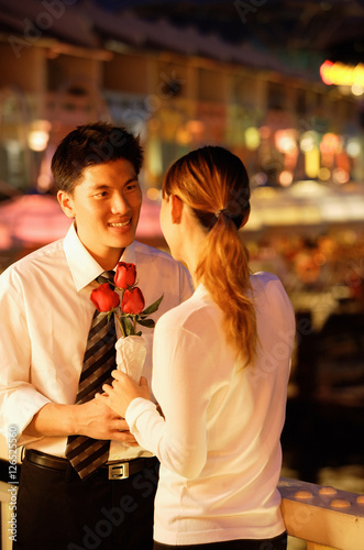 Couple standing face to face, woman holding roses