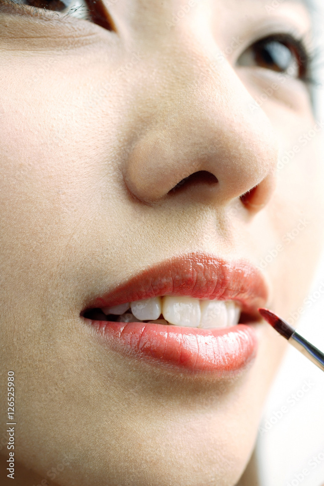 Woman putting on lipstick with lip brush, close up
