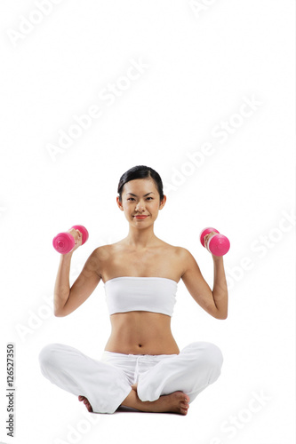 Woman sitting crossed legged on floor, lifting dumbbells