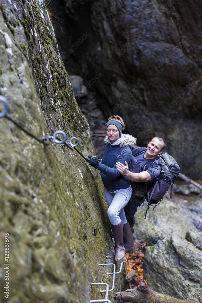 couple of hikers climbing on safety cables in a gorge above the