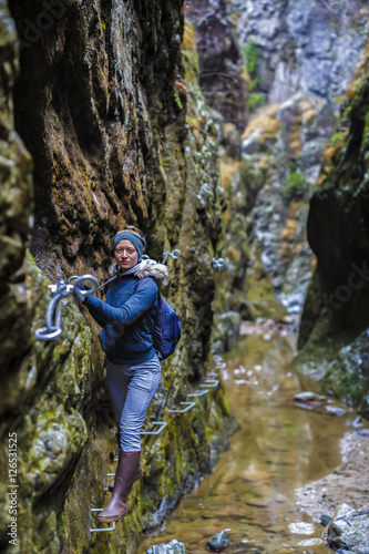 Woman hiker climbing on safety chains through a very narrow gorg