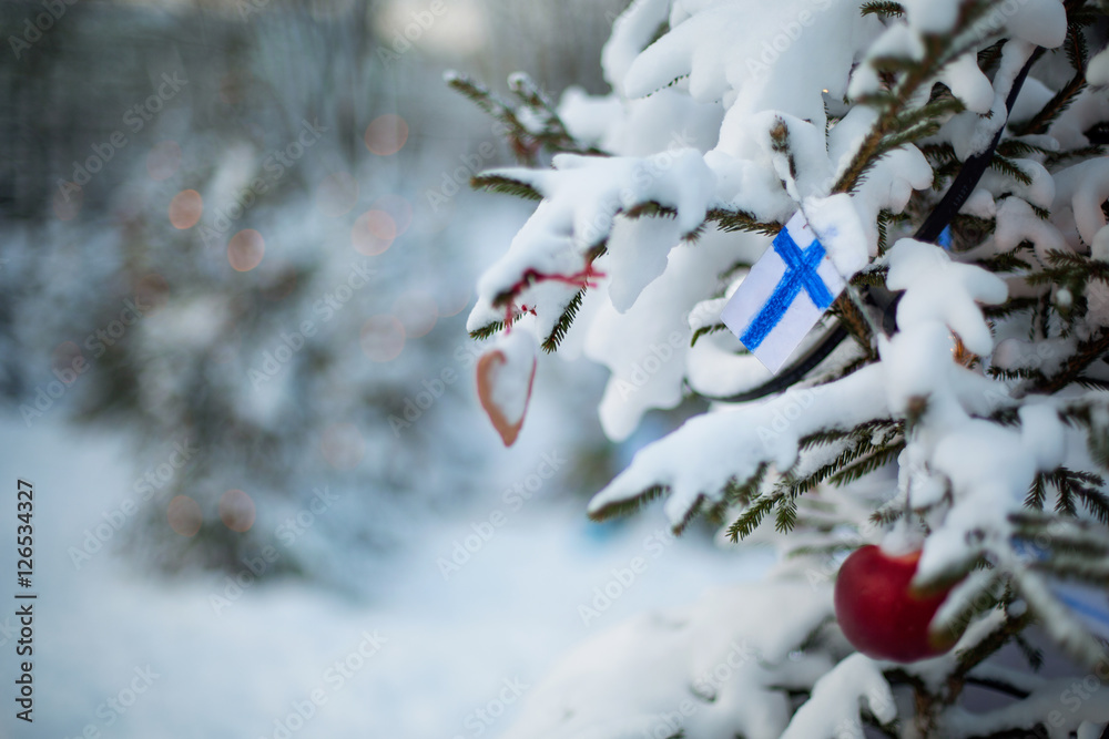 Finland Christmas holiday greetings card. Christmas tree covered with snow and a Finnish flag. Winter outdoor scene background