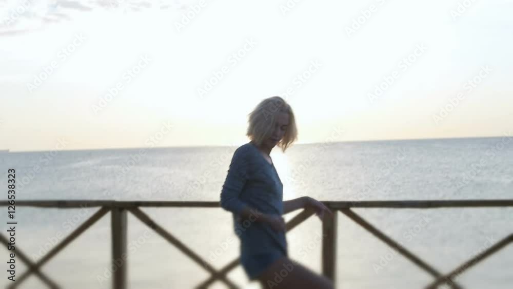 Blond girl in denim shorts dancing happy near the beach at beautuful sunrise Blond girl in denim shorts dancing happy near the beach at beautuful sunrise