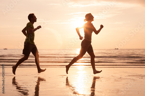 silhouette of beautiful couple jogging on sea beach at sunset, healthy lifestyle concept
