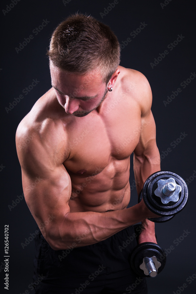 portrait of young muscular man doing exercises with dumbbells ov