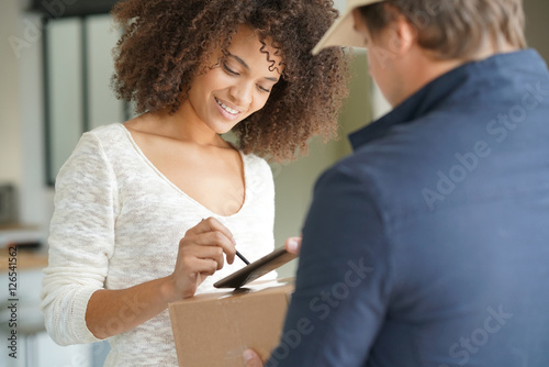 Fényképezés Mixed race woman receiving package from delivery man