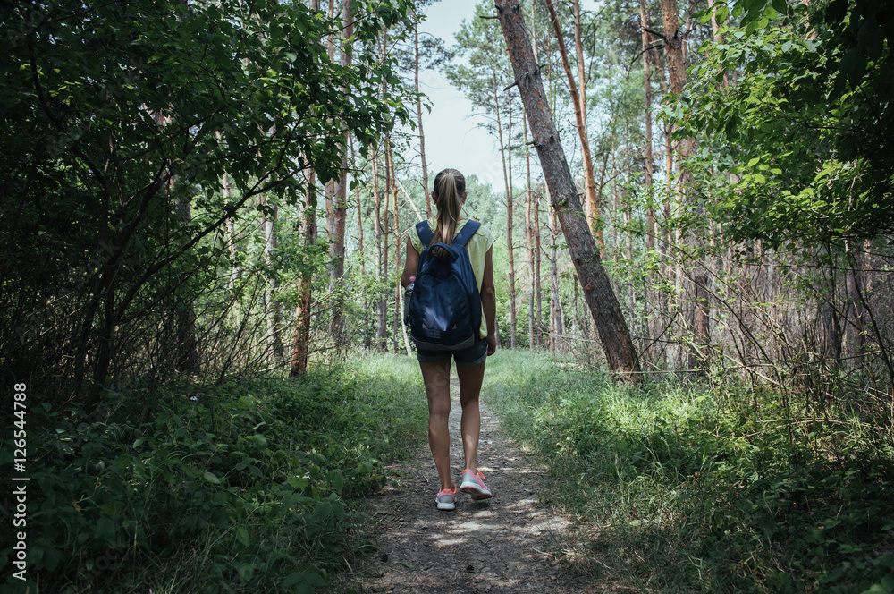 Active female hiker with backpack trekking through natural park in summer. Concept of camping, vacation and tourism. 