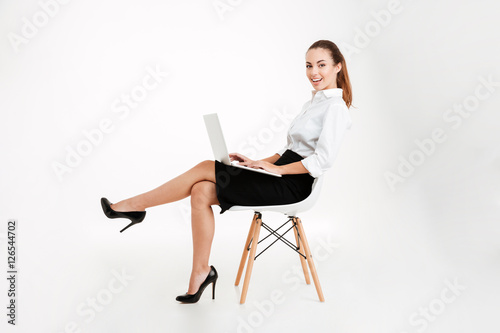 Happy young businesswoman sitting on the chair with laptop