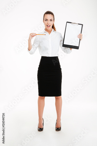 Smiling young businesswoman pointing pencil at blank clipboard