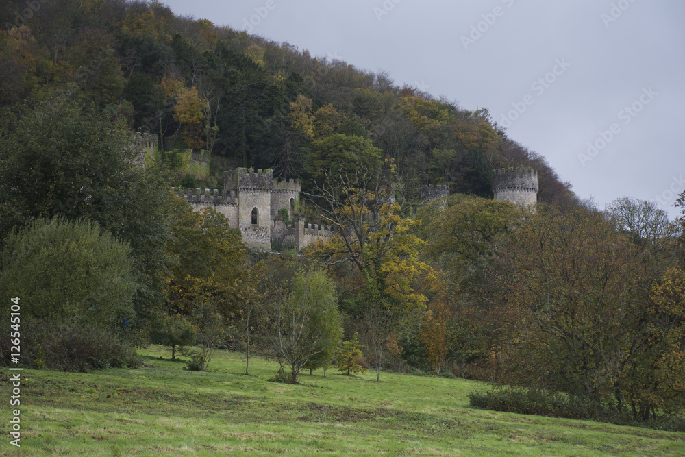 Gwrych Castle nestled in the trees on a hill side behind trees in Wales - European castle in the UK during Autumn - stormy weather and clouds