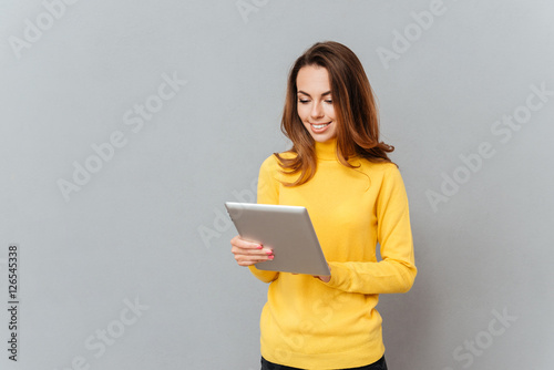 Smiling young woman in yellow sweater using tablet computer