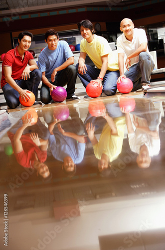 Four men in bowling alley, crouching, holding bowling balls