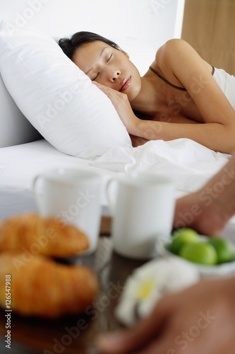 Woman sleeping in bed, man setting down breakfast tray