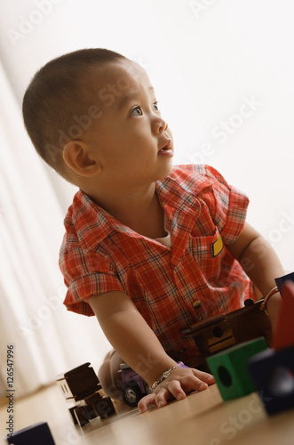 Young boy on floor, playing with toys, looking away