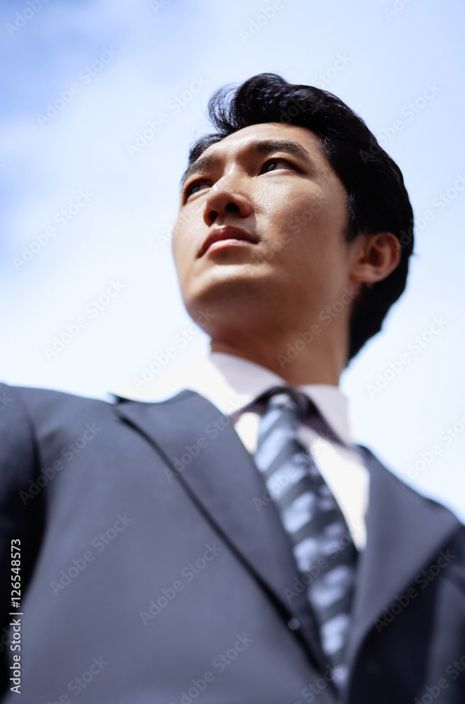 Businessman standing, looking away, low angle view Businessman standing, looking away, low angle view