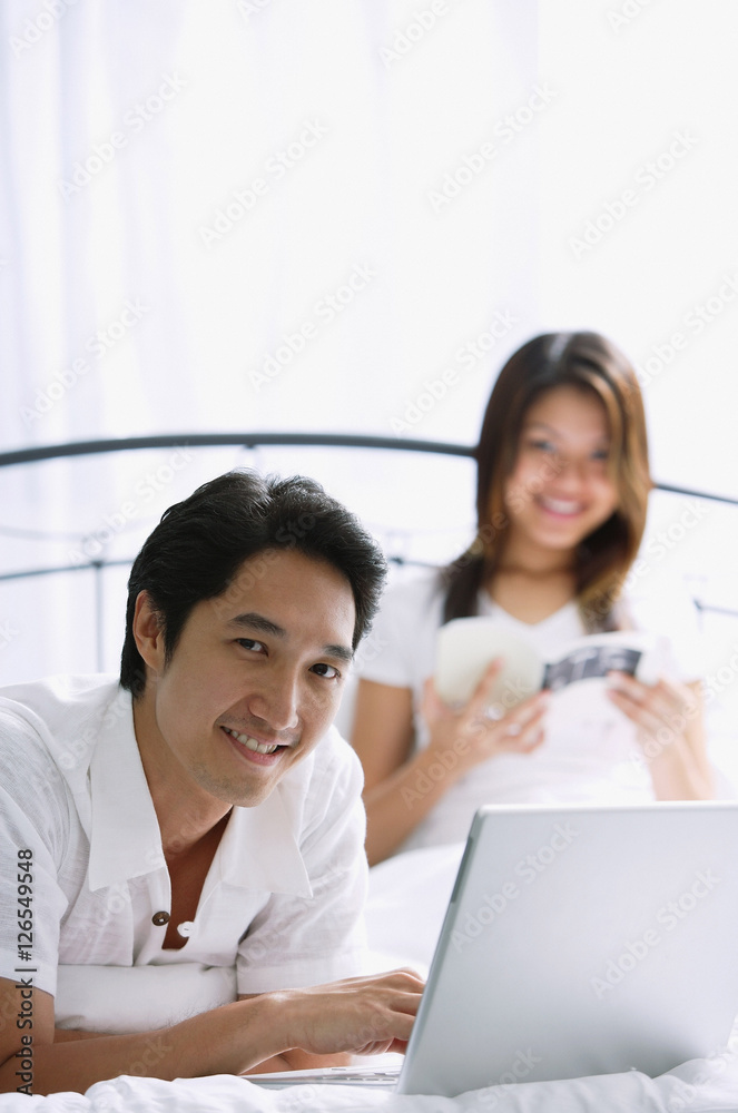 Couple in bedroom, man using laptop, smiling at camera Couple in bedroom, man using laptop, smiling at camera