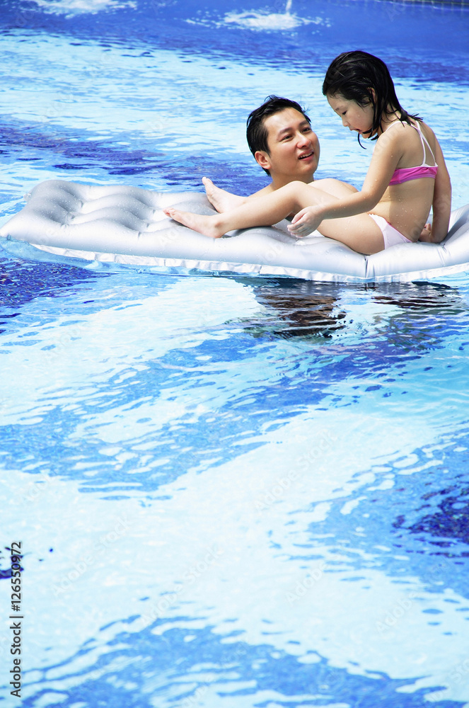 Father and daughter in swimming pool, daughter on inflatable raft Father and daughter in swimming pool, daughter on inflatable raft