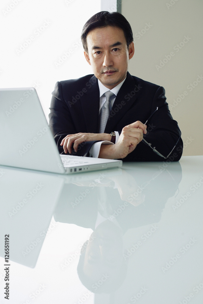 Businessman sitting at table, laptop next to him, looking at camera Businessman sitting at table, laptop next to him, looking at camera