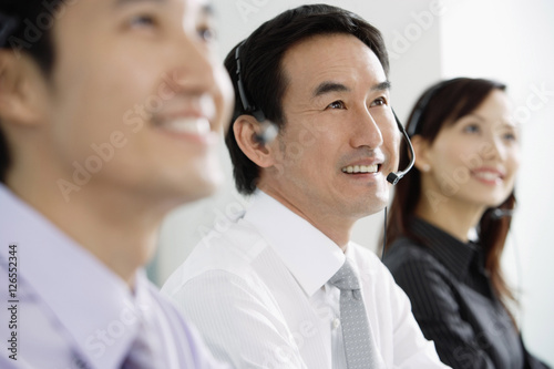 Executives in a row, wearing headsets, looking away, smiling