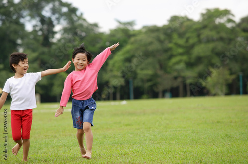 Two girls running on grass, side by side, arms outstretched