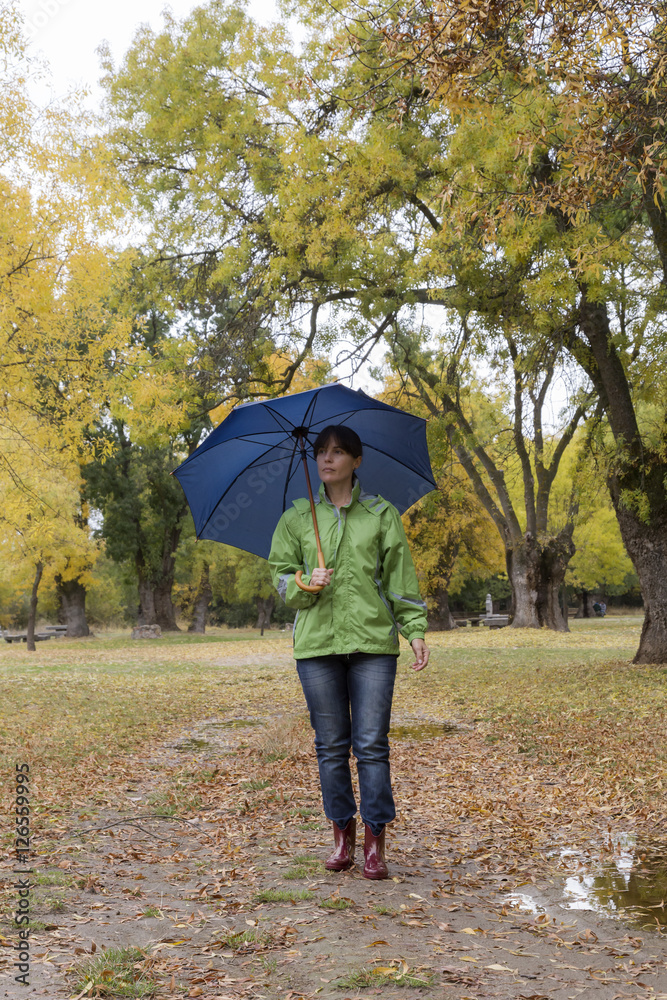 Woman walking with an umbrella in a park with yellow leaves falling from trees Woman walking with an umbrella in a park with yellow leaves falling from trees