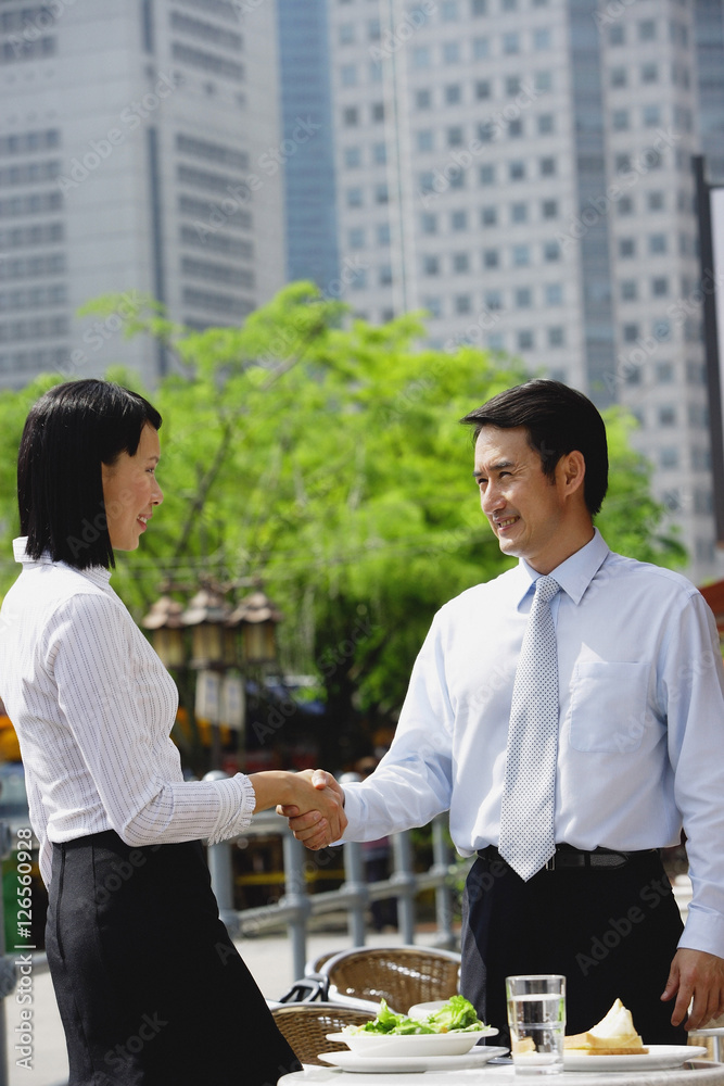 Businesswoman and businessman at outdoor cafe, shaking hands