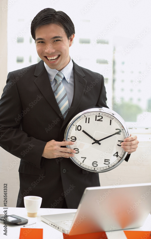 Businessman standing in front of desk, holding clock
