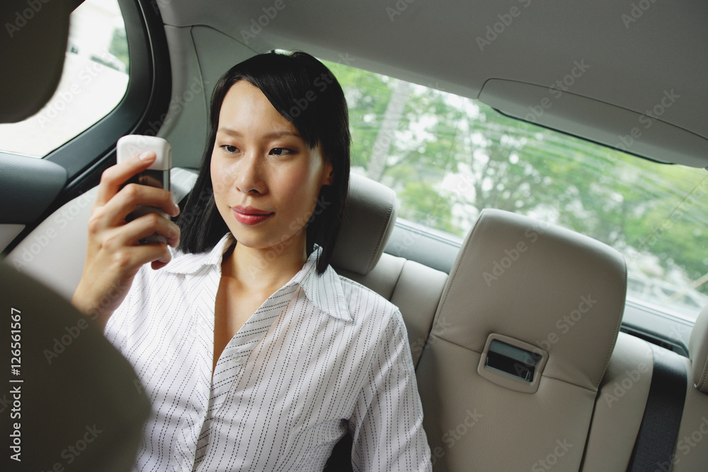 Businesswoman in backseat of car using mobile phone, text messaging