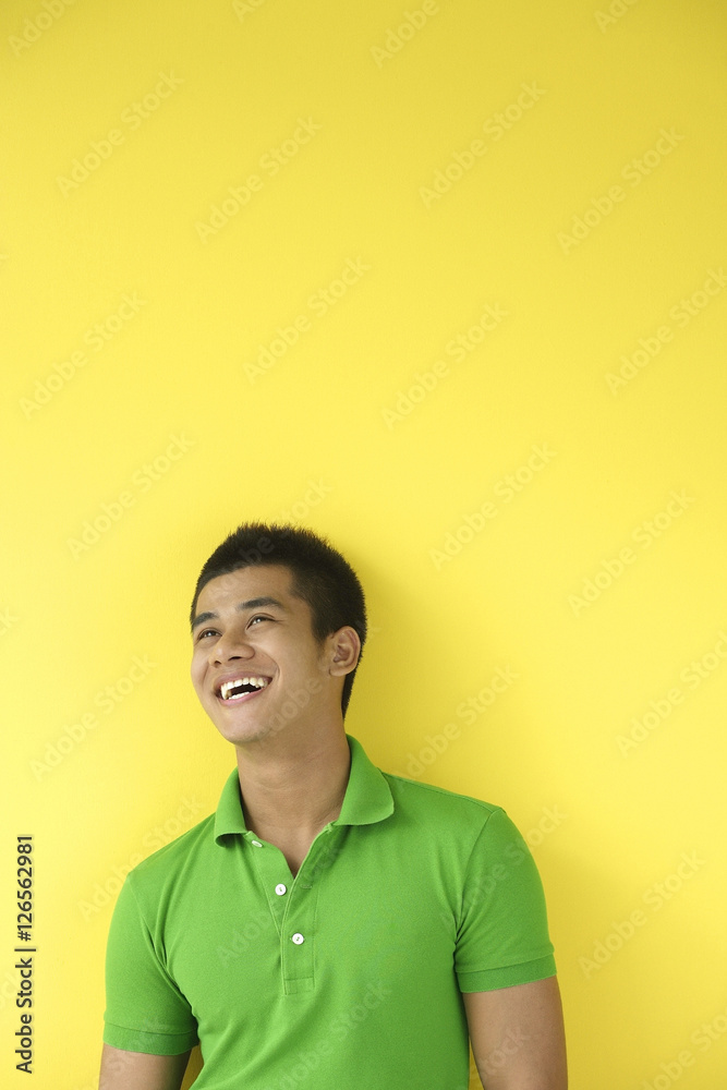 Obraz premium Man standing against yellow wall, smiling, looking up