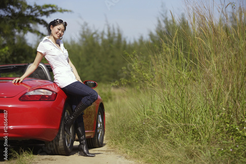 Woman leaning on red sports car, smiling at camera