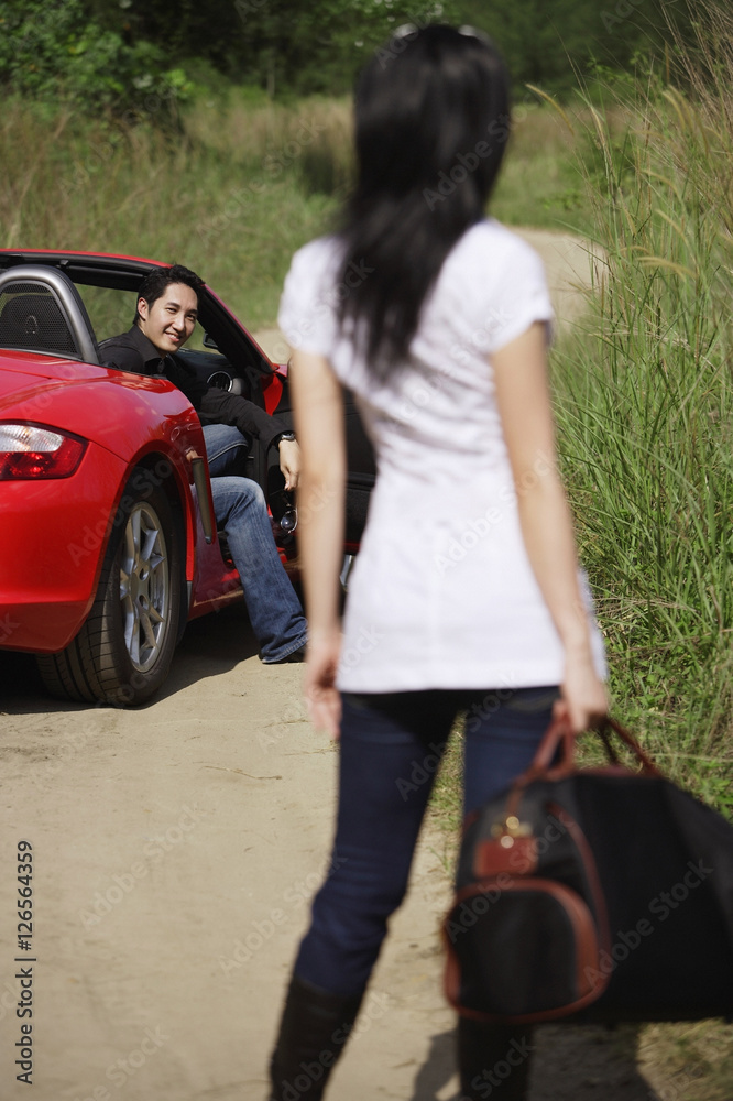 Woman standing on side of road, looking at man in red sports car