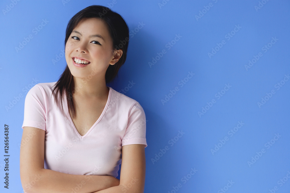 Young woman with arms crossed, standing against blue background Young woman with arms crossed, standing against blue background