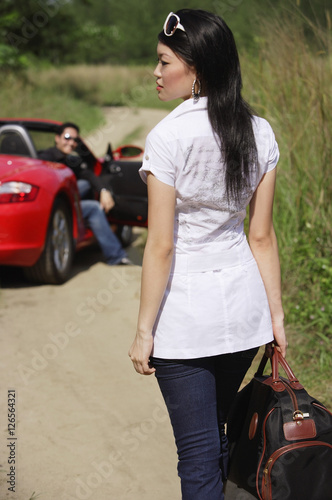 Woman with bag in foreground, man and red sports car in the background