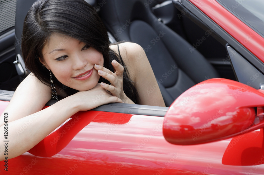Woman sitting in convertible, looking at herself in side view mirror