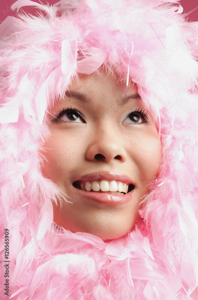 Woman with pink feathers around her face, looking up