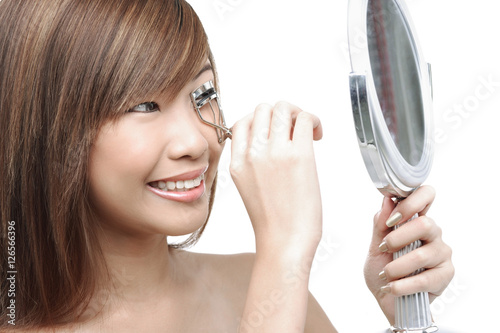 Teenage girl using eyelash curler, looking in mirror