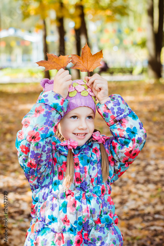 Веселая девочка держит кленовые листья над головой на фоне осеннего леса
