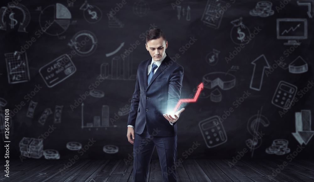 Businessman holding computer projection of rising red arrow on the background with economic sketches. Businessman holding computer projection of rising red arrow on the background with economic sketches.